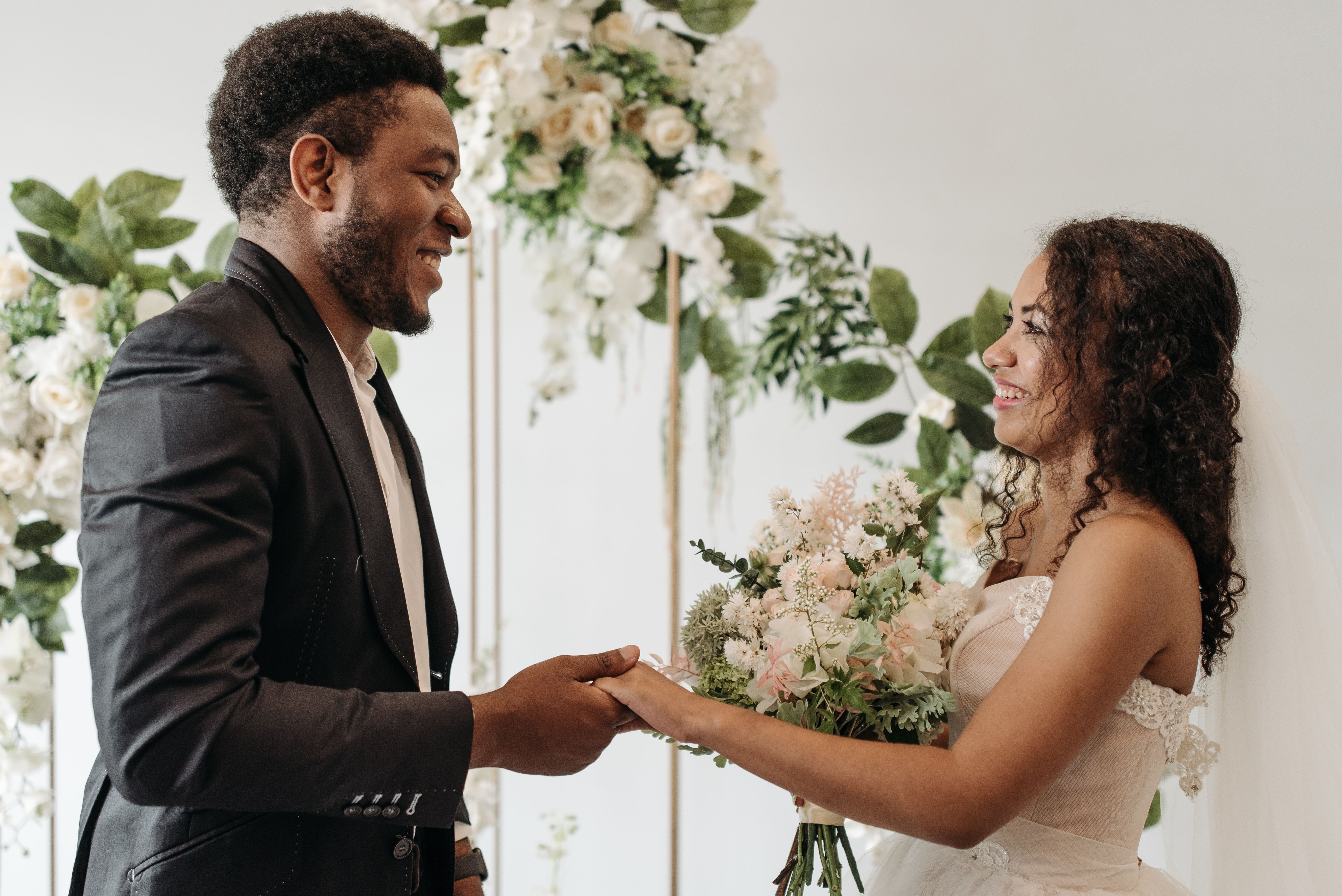 Couple holding hands beneath a white floral ceremony arch